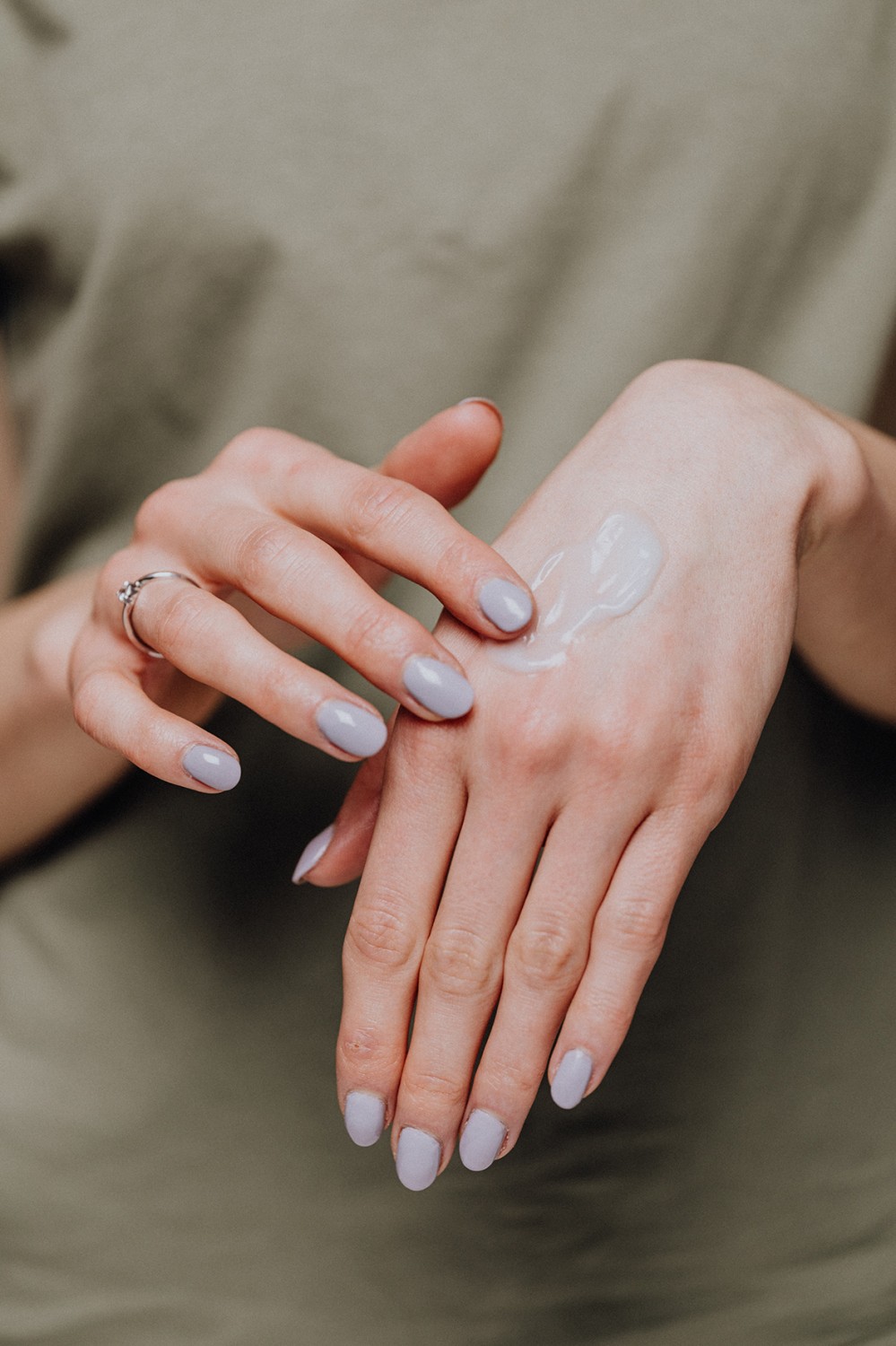 A woman in a green blouse and with green nail polish uses a body lotion made from natural raw materials.